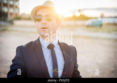 Lifestyle portrait of vintage looking young man in suit with sunglasses at sunset Stock Photo