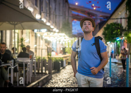 Young man in blue shirt walking on lively streets and looking up at the evening Stock Photo