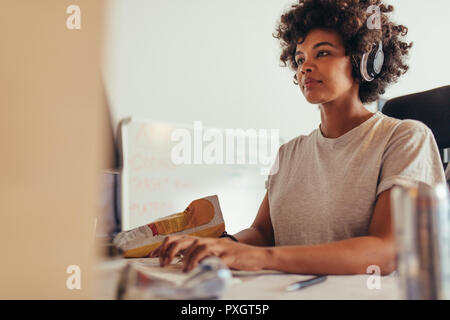 Female programmer typing data codes, working on project in software development company. African woman wearing headphones concentrating while working Stock Photo