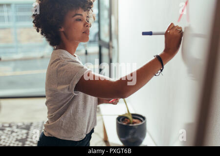 Young african businesswoman writing her ideas on a white board at office. Woman writing project plan on white board. Stock Photo