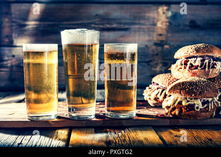 Street food. A three big burger with glasses of light beer. On a wooden background. close up. rustic style Stock Photo