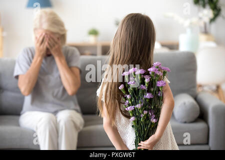 Little girl making surprise for grandmother holding flowers Stock Photo