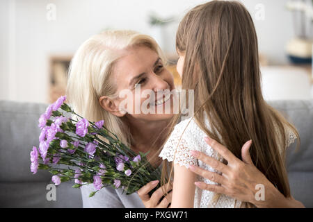 Happy grandmother hug small granddaughter thanking for flowers Stock Photo