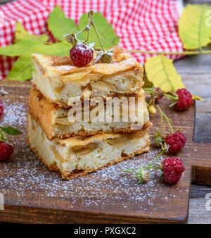 baked square pieces of apple pie are stacked on a brown wooden board, sponge cake Stock Photo