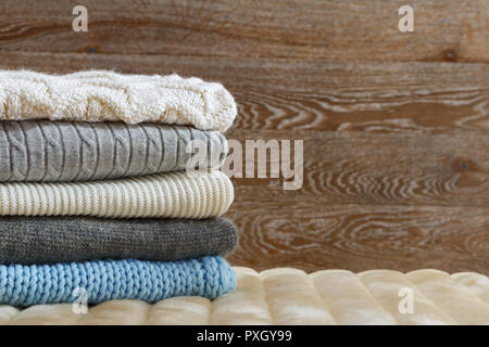 Warm clothing lies in a pile on a fluffy soft rug. Knitted sweaters on a wooden background. Autumn and winter concept Stock Photo