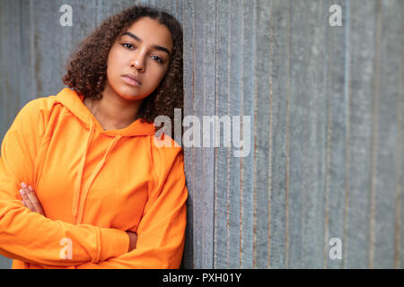 Beautiful mixed race African American girl teenager female young woman outside wearing an orange hoodie looking sad depressed or thoughtful Stock Photo