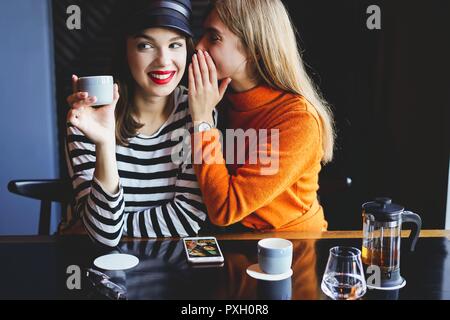 communication and friendship concept - smiling young women with coffee cups at cafe. Stock Photo