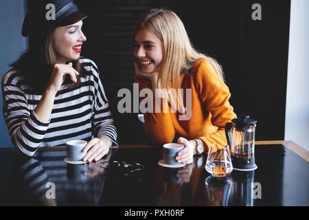 communication and friendship concept - smiling young women with coffee cups at cafe. Stock Photo