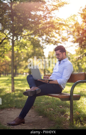 Handsome young businessman working on his laptop in the park at sunset Stock Photo