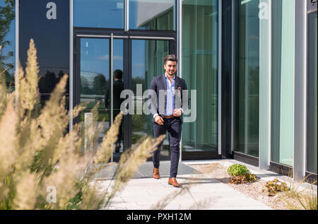 Handsome young businessman walking out of an office building being serious Stock Photo