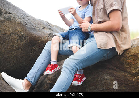 cropped image of father and son using smartphone on stones at park Stock Photo