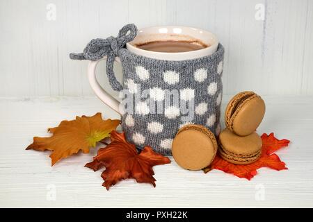 hot chocolate drink in mug with gray and white polka dot knitted sweater and macaroons on autumn leaves Stock Photo