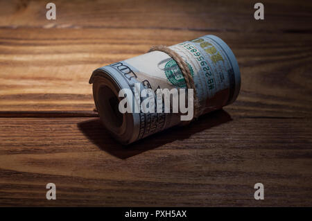 A roll of dollarson a wooden textured table in the dark illuminated by a ray of light. Stock Photo