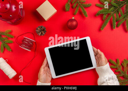 Top view of tablet computer in woman hands. Christmas decoration and fir branches on red background Stock Photo