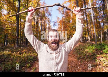 Young man in autumn forest shouting and holding wood branch Stock Photo