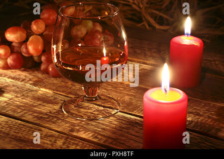 christmas candles, grapes and glass with cognac or whisky on wood background. Christmas decoration. Stock Photo
