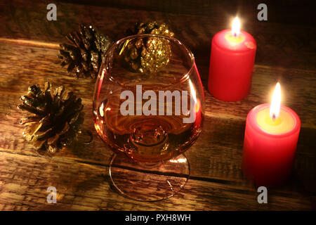 christmas candles and glass with cognac or whisky on wood background. Christmas decoration. Stock Photo