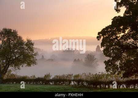 Mist and fog at sunrise rolling over the countryside around the cotswold village of Lower Slaughter in autumn. Cotswolds, Gloucestershire, England Stock Photo