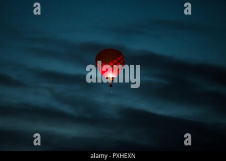 Colorful hot air balloon in dark pink and purple colors glowing in a dark blue early morning sky with dramatic clouds Stock Photo