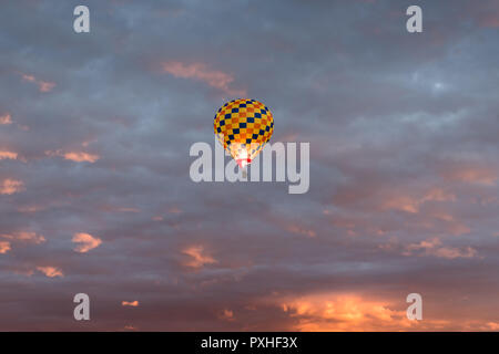 Colorful hot air balloon in yellow, orange, and dark blue colors glowing against a dramatic colorful sky and clouds at sunrise