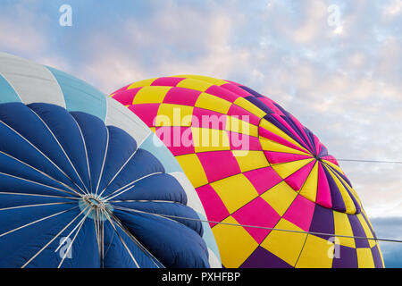 Colorful hot air balloons in vibrant colors of blue, purple, pink, and yellow  being inflated under an beautiful early morning sky at sunrise Stock Photo