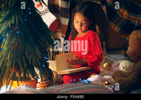 Merry Christmas and Happy Holidays. The happy girl reading a book in the winter at home. The holiday, childhood, winter, celebration concept Stock Photo