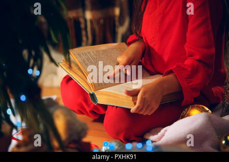 Merry Christmas and Happy Holidays. The happy girl reading a book in the winter at home. The holiday, childhood, winter, celebration concept Stock Photo