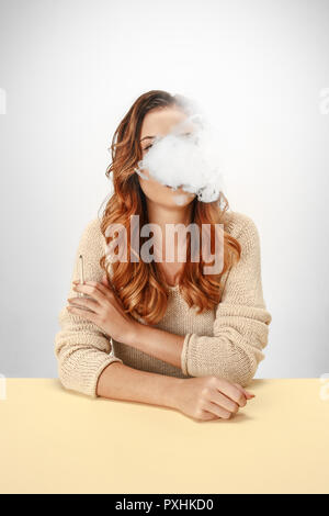 Tranquil woman sitting and smoking at the table. Cloud of smoke covering her face. Copy space. Isolated on white background. Trendy colors Stock Photo