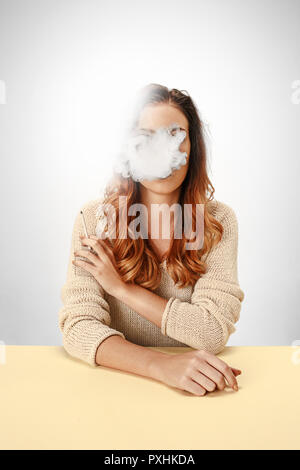 Tranquil woman sitting and smoking at the table. Cloud of smoke covering her face. Copy space. Isolated on white background. Trendy colors Stock Photo