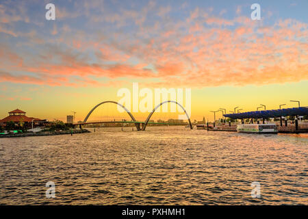 Scenic landscape of Elizabeth Quay Bridge on Swan River in Elizabeth Quay marina. The arched bridge is a new tourist attraction in Perth, Western Australia. Sky with red clouds of sunset. Stock Photo