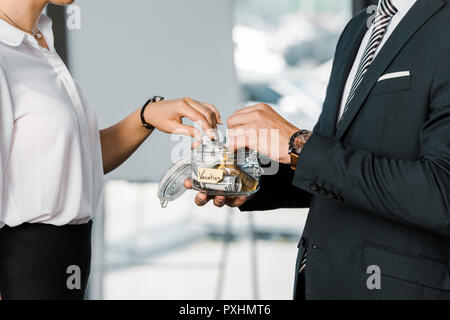 cropped shot of business colleagues putting money into glass jar with vacation lettering in office Stock Photo