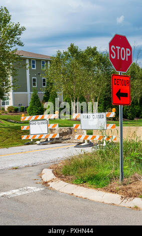 Vertical shot of detour and road closed signs on a road deadending into an apartment complex under cloudy skies. Stock Photo