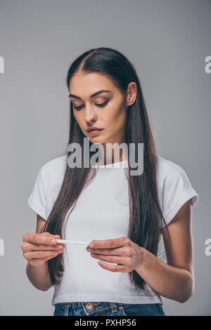 upset young woman holding pregnancy test isolated on grey Stock Photo