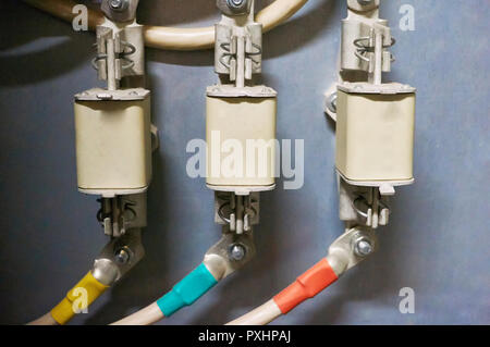 Three trains of high-voltage fuses are connected to the multi-colored wires. Industrial background. Stock Photo
