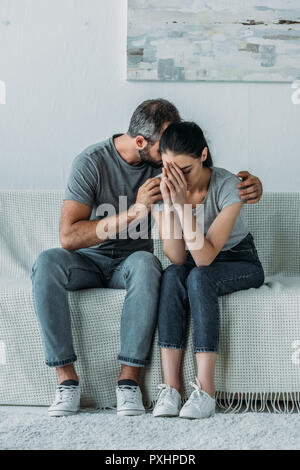upset young man supporting depressed girlfriend while sitting together on couch Stock Photo