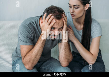 young woman supporting depressed frustrated boyfriend sitting on couch Stock Photo