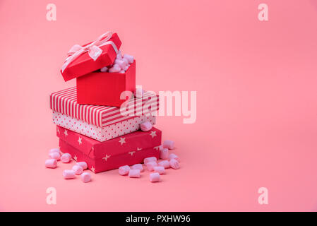 Christmas gifting theme image with a stack of gifts wrapped in different red designs, full of pink tiny marshmallows, on a pink paper background. Stock Photo