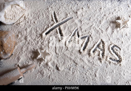 The word 'Xmas' written in white flour on a kitchen table prepared for baking gingerbread cookies Stock Photo