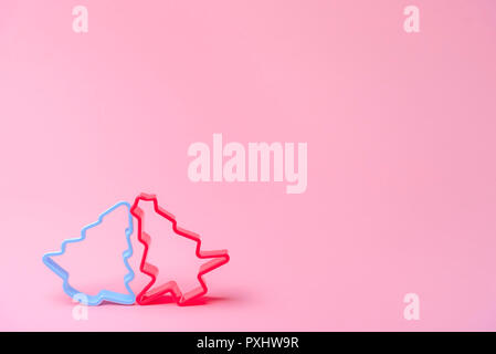 Christmas sweets baking concept with two cookies cutters, in red and blue, leaned against each other on a pink paper background. Minimal image. Stock Photo