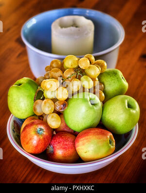 bowl of apples and grapes with candle on wooden table Stock Photo