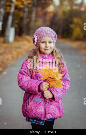 Little girl on a walk on a sunny autumn day holding orange maple leaves in her hands and smiling. Outdoor. Portrait Stock Photo