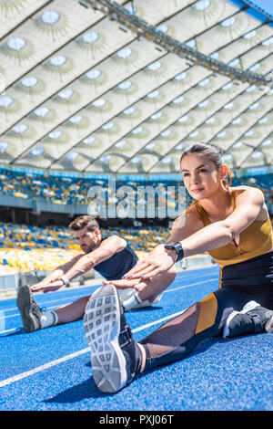 young attractive couple sitting on running track and stretching at sports stadium Stock Photo