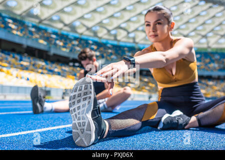 young active couple sitting on running track and stretching at sports stadium Stock Photo