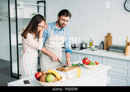 boyfriend cutting onion and crying girlfriend leaning on him in kitchen Stock Photo