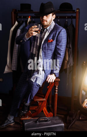 Elegant man in fashion suit and hat posing at atelier with beverage Stock Photo