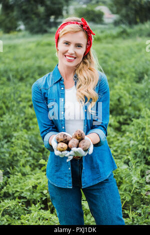 smiling attractive farmer holding ripe potatoes in field at farm Stock Photo