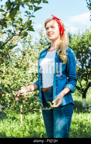 attractive farmer touching tree in apple garden at farm and looking away Stock Photo