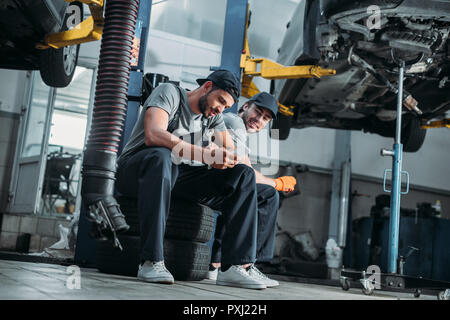 two auto mechanics using smartphone and resting in auto repair shop Stock Photo