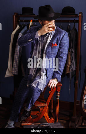 Elegant man in fashion suit and hat posing at atelier with beverage Stock Photo