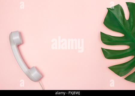 Traditional phone receiver and Monstera palm leaf on pastel pink background, with copy space. Stock Photo